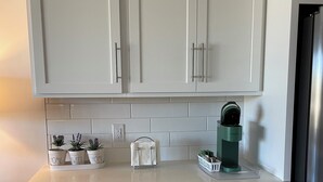 Una cocina con armarios blancos, una encimera y una cafetera verde.
