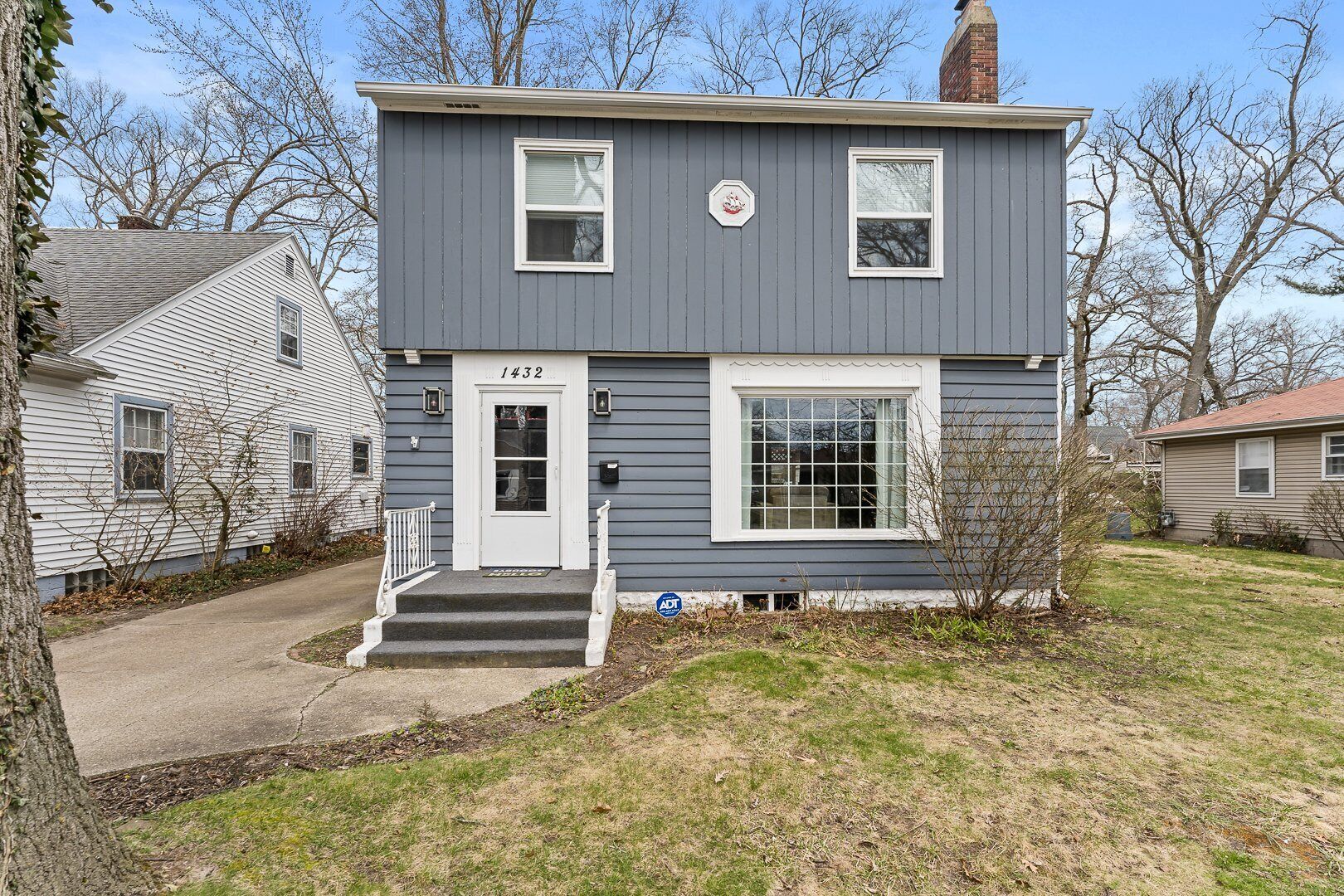 A two-story house with a gray exterior, a white front door, and a small front yard.
