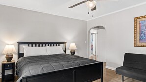 Een moderne slaapkamer met een donker bed, twee bedlampen, een plafondventilator en een ingelijste afbeelding aan de muur.