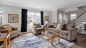 Een woonkamer met een bank, fauteuil, salontafel en een trap.