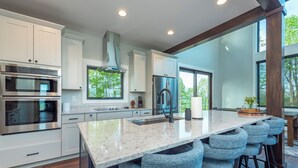 A modern kitchen with white cabinetry, stainless steel appliances, a granite countertop, and a bar area with stools.