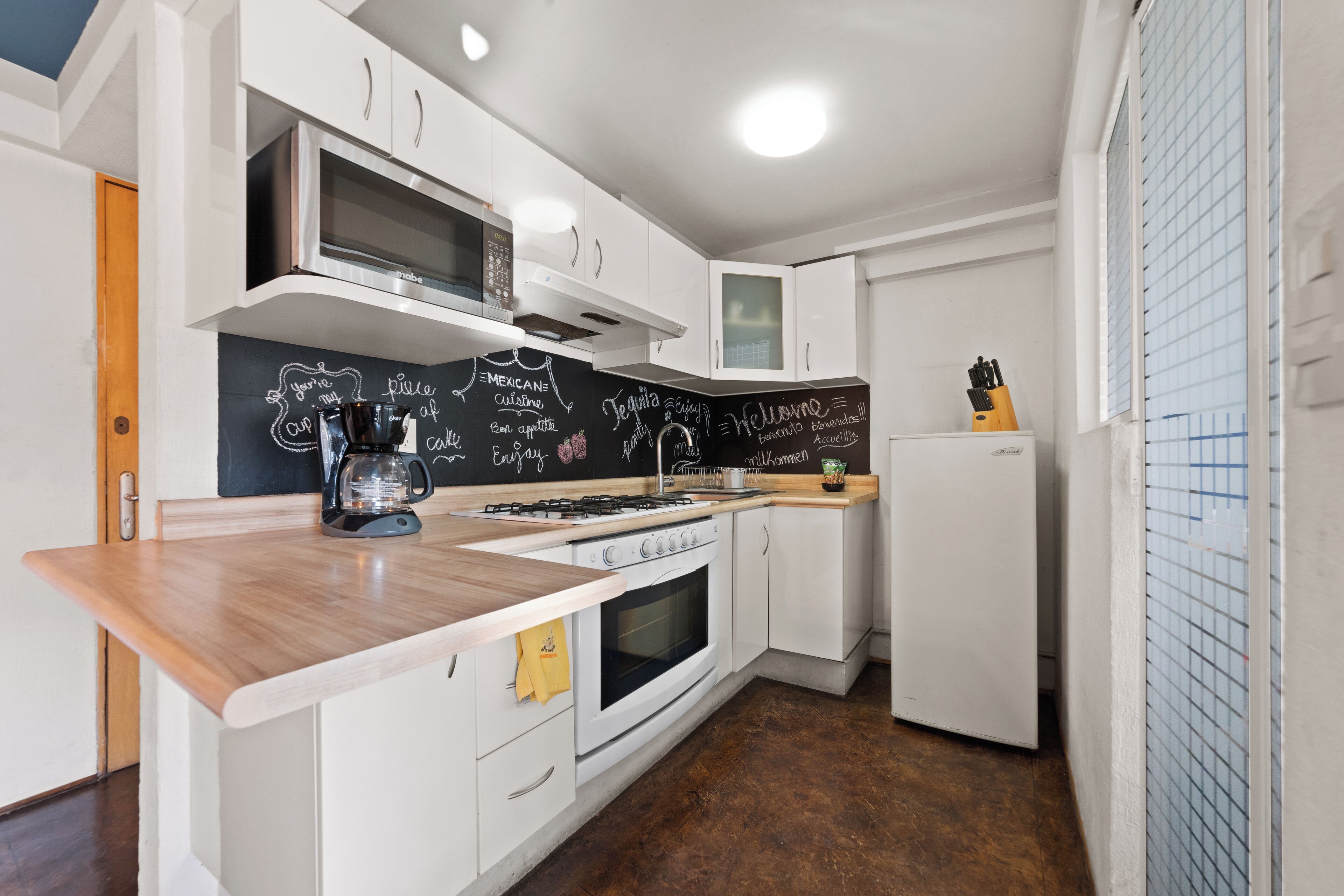 A modern kitchen with white cabinetry, a blackboard with Mexican cuisine notes, a coffee maker, and a refrigerator.
