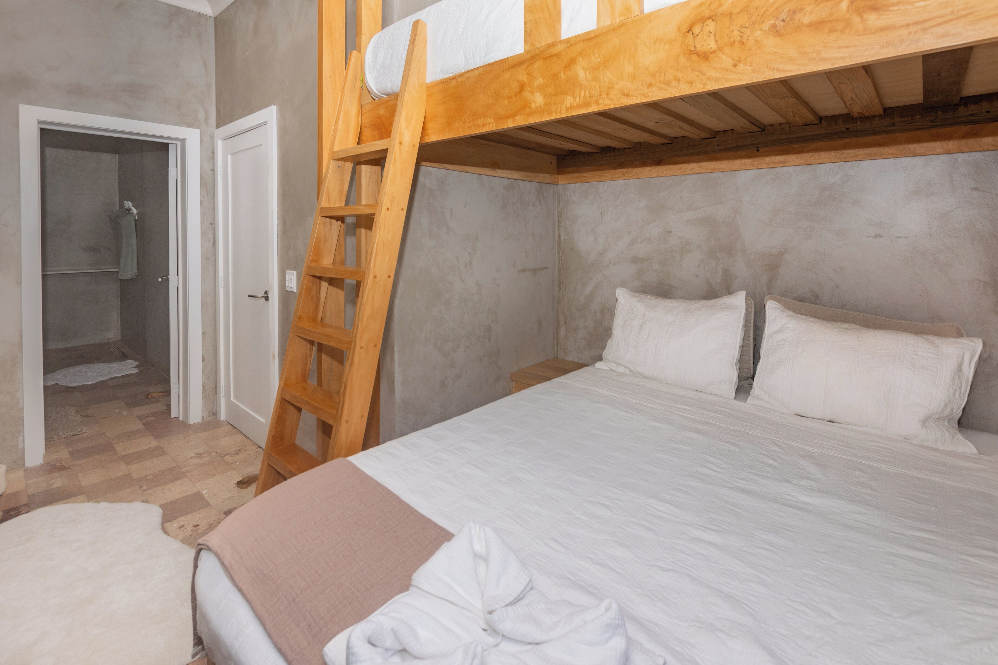 A bunk bed with a wooden ladder, a white bedspread, and a white pillow.