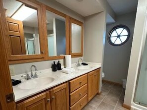 A bathroom with wooden cabinets, a double sink, and a round window. - Charming Farmhouse 10 acres near MidOH Race, Clear Fork & Mt Gilead State Parks (Galion)