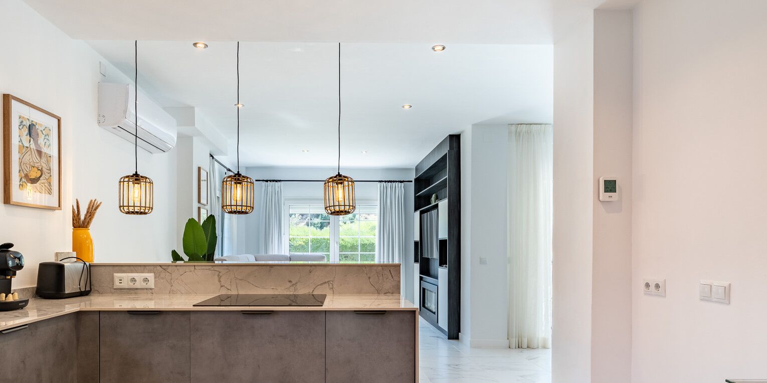 A modern kitchen with a marble countertop, pendant lights, and a view to the dining area.