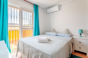A bedroom with a bed, a nightstand, a lamp, a window with curtains, and an air conditioning unit.