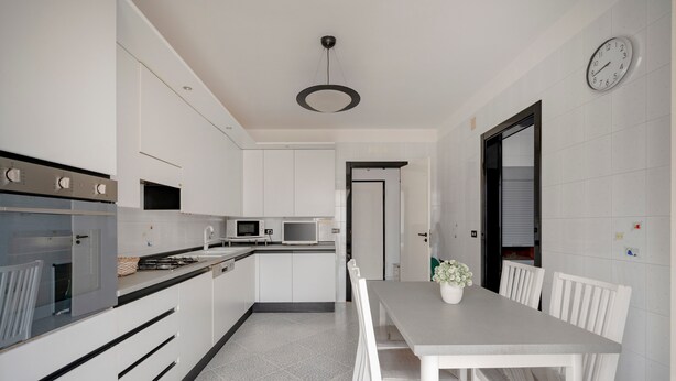 A modern kitchen with white cabinets, a dining table with chairs, a clock on the wall, and a ceiling light fixture. - Apartment 'Profumo Di Mare' with Sea View, Wi-Fi, and Air Conditioning (Polignano a Mare)