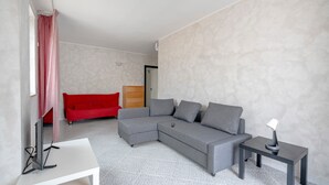 A modern living room with a grey sectional sofa, a red sofa, a white TV stand, and a small table with a lamp. - Apartment 'Profumo Di Mare' with Sea View, Wi-Fi, and Air Conditioning (Polignano a Mare)