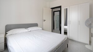 A bedroom with a bed, a wardrobe, a nightstand, and a standing fan. - Apartment 'Profumo Di Mare' with Sea View, Wi-Fi, and Air Conditioning (Polignano a Mare)