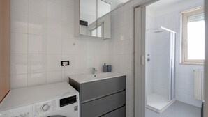A modern bathroom with a washing machine, a mirror, a sink, and a shower. - Apartment 'Profumo Di Mare' with Sea View, Wi-Fi, and Air Conditioning (Polignano a Mare)