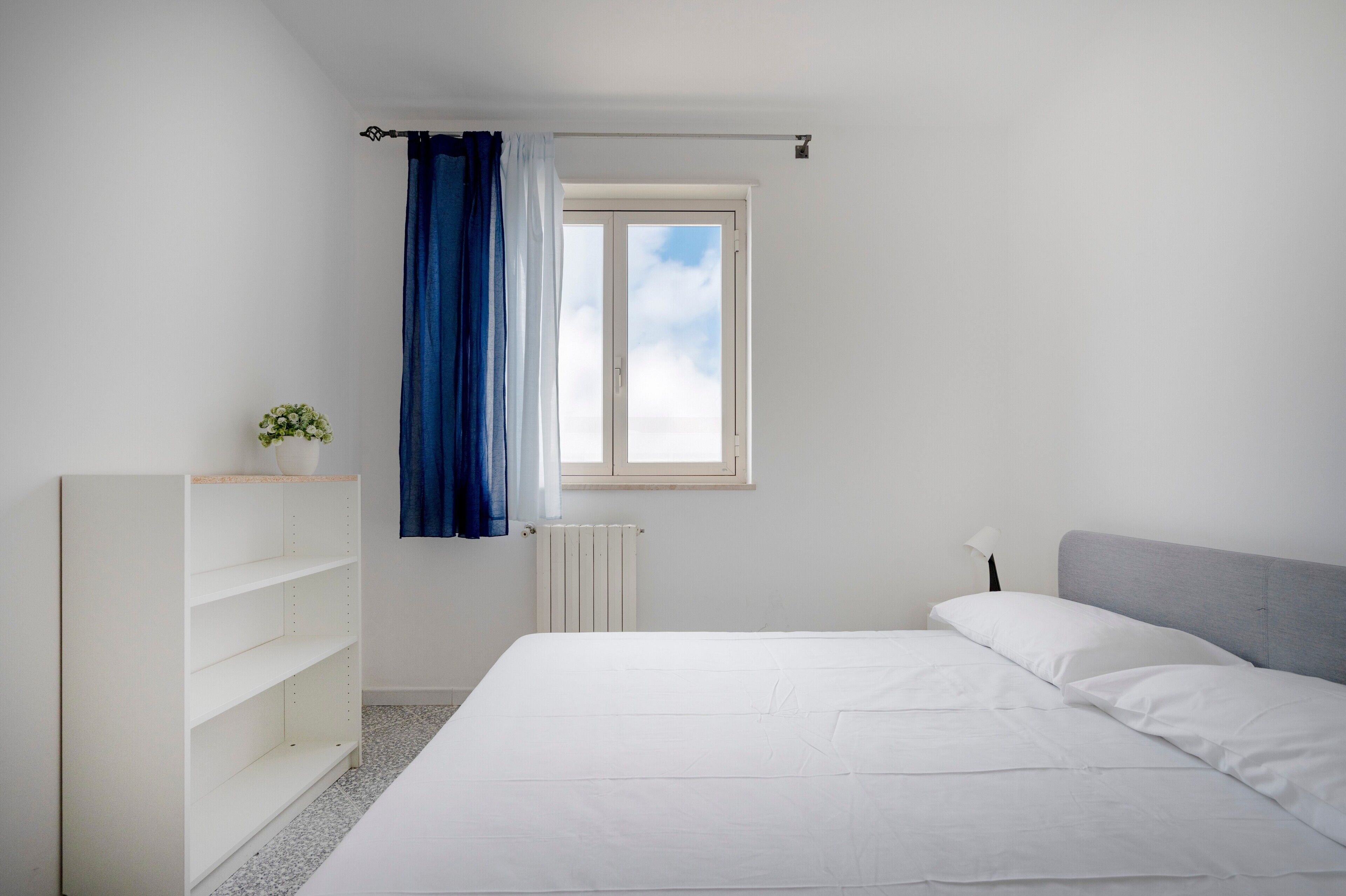 A bedroom with a bed, a white wardrobe, a radiator, and a window with curtains.