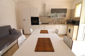 A modern kitchen with white cabinets, a built-in oven, microwave, and a dining area with a white table and two wooden placemats.