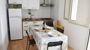 A compact kitchen with white cabinets, a gas stove, a sink, and a dining table set for two.