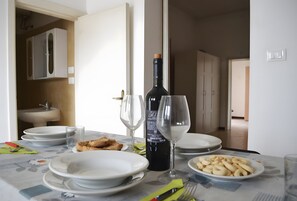 Una mesa de comedor con platos, vasos, una botella de vino y comida.