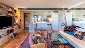 Een moderne woonkamer met een flatscreen televisie, een bank, een salontafel en een keuken op de achtergrond.