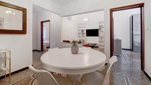 A dining area with a round table, white chairs, a vase with flowers, and a chandelier. - Cruise Apartment with Private Terrace, Balcony, and Wi-Fi (Savona)