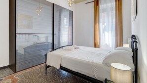 A hotel room with a bed, a large mirror, a chandelier, and a window with curtains. - Cruise Apartment with Private Terrace, Balcony, and Wi-Fi (Savona)