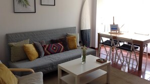 A living room with a grey sofa, a white coffee table, and a dining area with a round table and chairs.