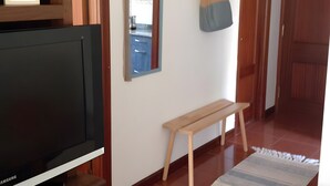 A living room with a flat-screen TV, a wooden bench, a mirror, a coat rack, and a hanging bag.