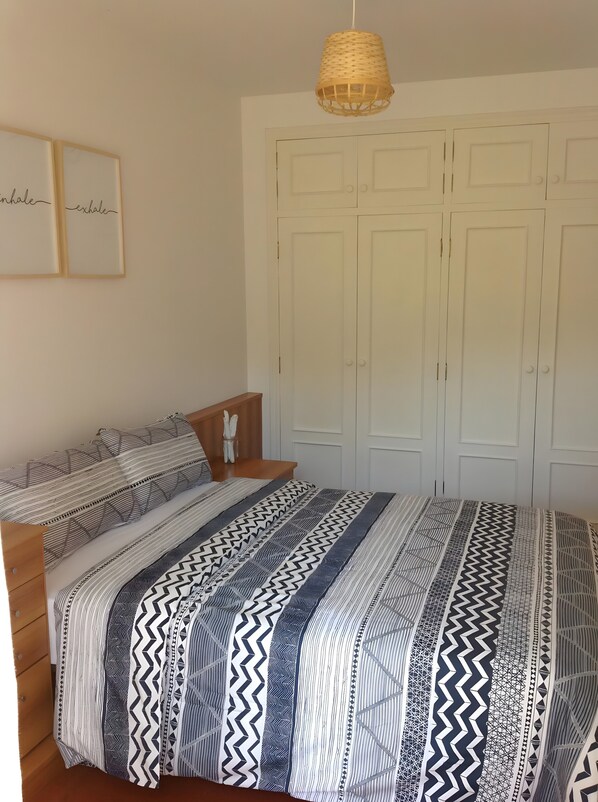 A bedroom with a bed, a bedside table, a hanging light fixture, and a wardrobe.