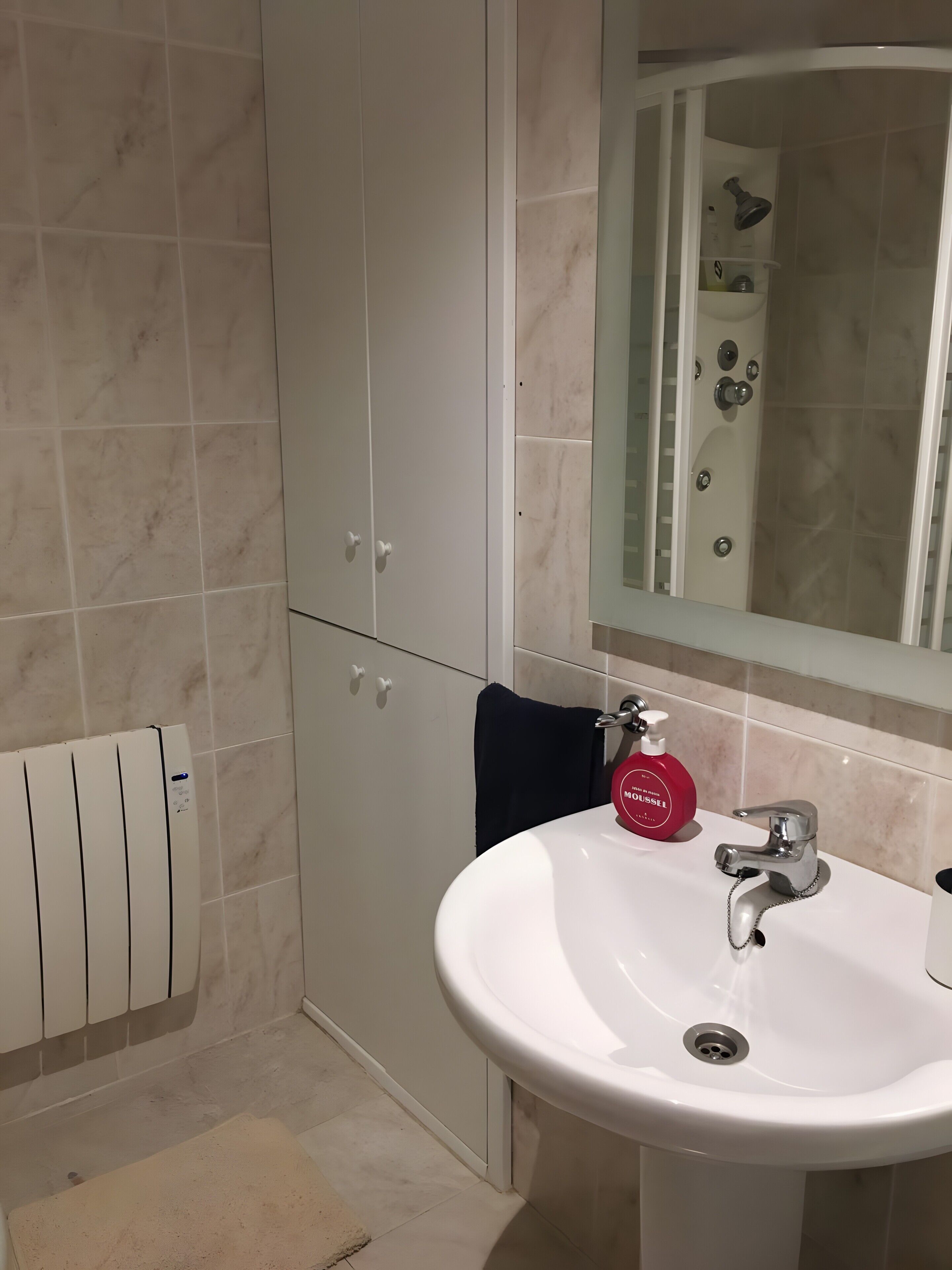 Een badkamer met een wit wastafel, een spiegel, een douche en een handdoekhouder.