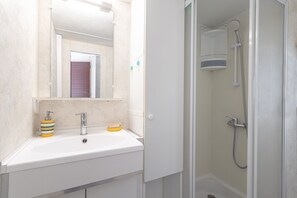A bathroom with a white sink, a mirror, a shower, and a door.