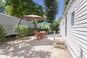 A patio area with a table and chairs, surrounded by gravel and greenery. - Mobile Home at Camping Le Front De Mer – Excludes Camping Fees – Shared Pool & Air Conditioning (Argelès-sur-Mer)