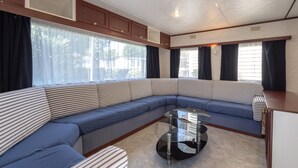 Un intérieur de camping-car moderne, avec un canapé modulable, une table basse en verre et de grandes fenêtres.