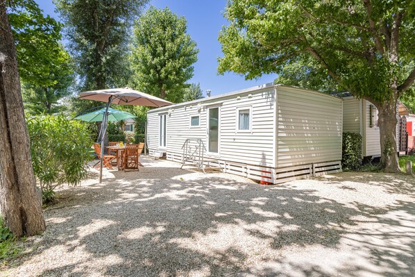 A mobile home with a patio area, outdoor furniture, and a tree. - Mobile Home at Camping Le Front De Mer – Excludes Camping Fees – Shared Pool & Air Conditioning (Argelès-sur-Mer)