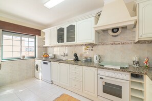 Una cocina con armarios blancos, lavadora, estufa y ventana con vistas.