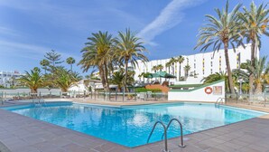 A swimming pool with palm trees, a lifebuoy, and a building in the background.