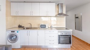 A compact kitchen with a washing machine, microwave, oven, and stainless steel appliances.