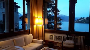 A room with a sofa, a lamp, and a view of a lake and mountains. - Apartment 'Tarlarini' with Private Terrace, Private Garden and Wi-Fi (Laveno-Mombello)