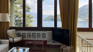 A room with a large window, a chair, a TV, and a radiator. - Apartment 'Tarlarini' with Private Terrace, Private Garden and Wi-Fi (Laveno-Mombello)