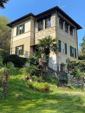 Un bâtiment à deux étages doté d’un balcon, d’un escalier en pierre et d’une végétation luxuriante.