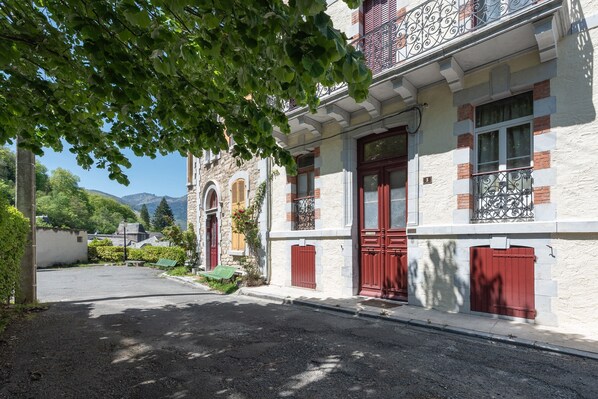 Un immeuble avec des portes rouges, un balcon orné de balustrades en fer forgé et une façade en pierre.