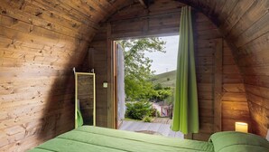 Quarto de cabana de madeira com uma cama, uma janela e vista para um jardim.