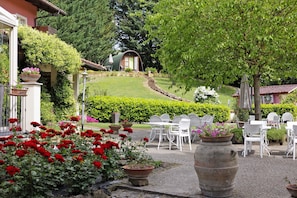 Un jardín con sillas blancas, un edificio pequeño y flores rojas.