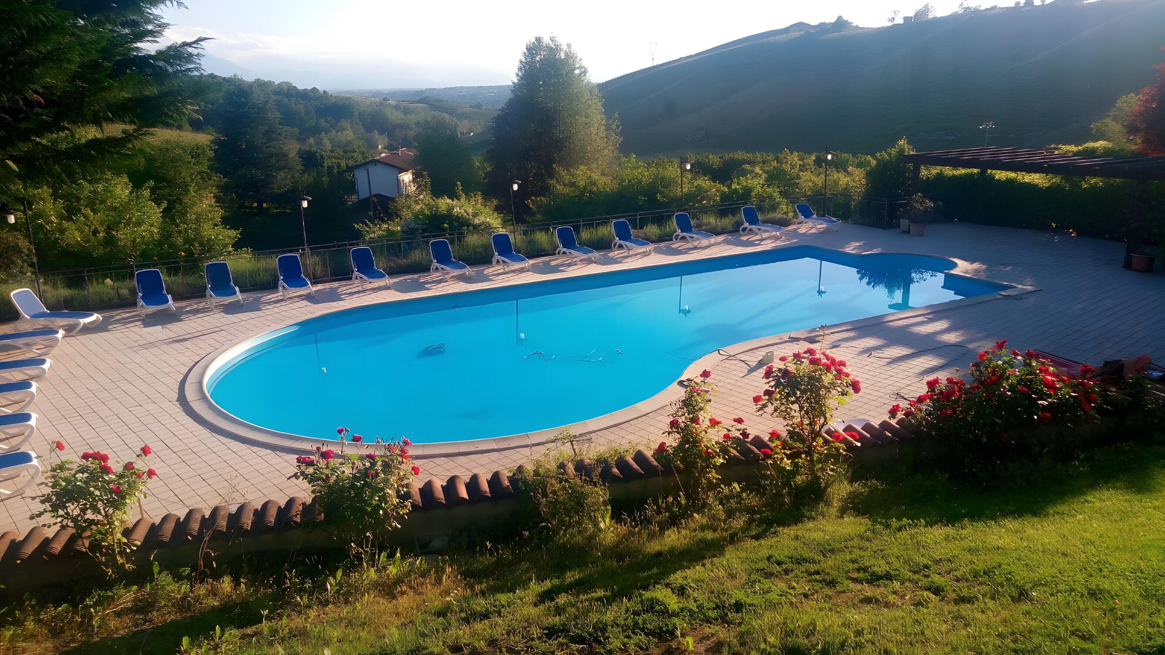 Una piscina con sillas de descanso, rodeada de vegetación y colinas.