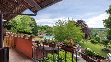 A balcony with potted plants, a pool, and a view of a green landscape.