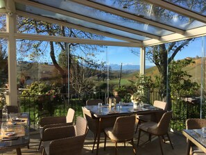 Un espace de restauration extérieur abrité, avec une table et des chaises, de grandes fenêtres et une vue sur la campagne.