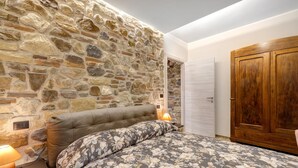 Una camera da letto con parete in pietra, un letto con biancheria da letto floreale, un armadio in legno e un comodino con lampada.