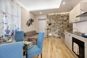 A compact living space with a dining area, a sofa, a kitchen with a stone wall, and a ceiling light.
