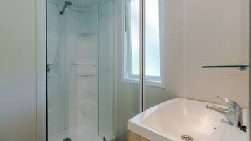 A bathroom with a glass-enclosed shower, a white sink with a modern faucet, and a window providing natural light.