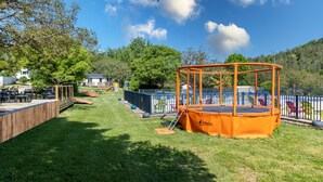 A playground with a trampoline, fenced area, and picnic tables. - 3★ Campsite in Périgord Noir – Mobile Home with Pool, Fishing & Family Activities (Saint-Martial-de-Nabirat)