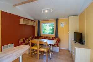 Une pièce de taille modeste, avec une table en bois, un banc, un téléviseur et une fenêtre donnant sur un paysage verdoyant.