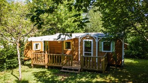 A wooden cabin with a porch, surrounded by trees. - 3★ Campsite in Périgord Noir – Mobile Home with Pool, Fishing & Family Activities (Saint-Martial-de-Nabirat)