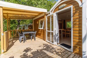 Une terrasse en bois avec une table et des chaises, un espace abrité et l’entrée d’un bâtiment avec une enseigne.