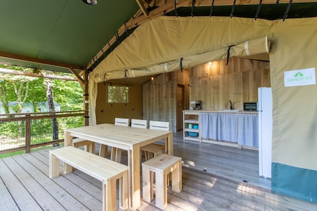 A wooden deck with a table and benches, a kitchen area with a refrigerator, and a sign for 'SANDERS.'. Caravan 'Lodge 8 Personnes' with Shared Pool, Private Terrace and Wi-Fi