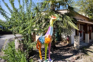 A colorful giraffe statue in a garden with a house in the background.